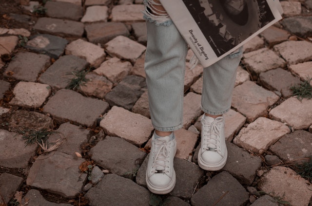 Person Wearing Blue Ripped Jeans and Pair of White Shoes holding newspaper