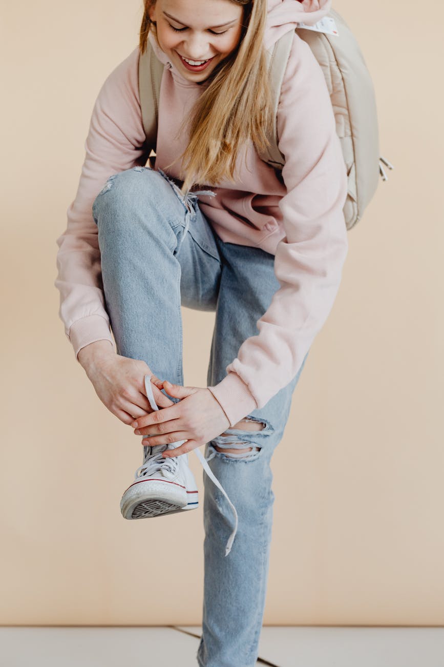 young woman in hoodie sweater and blue denim jeans tying her shoes